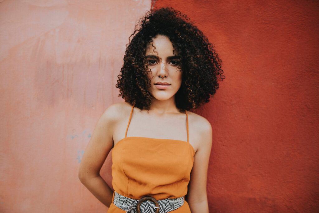 Lady poses in front of colourful wall with tight curly hair